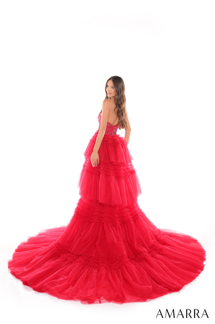 A woman wears a tiered, bright red tulle ball gown with a dramatic, voluminous skirt and train.
