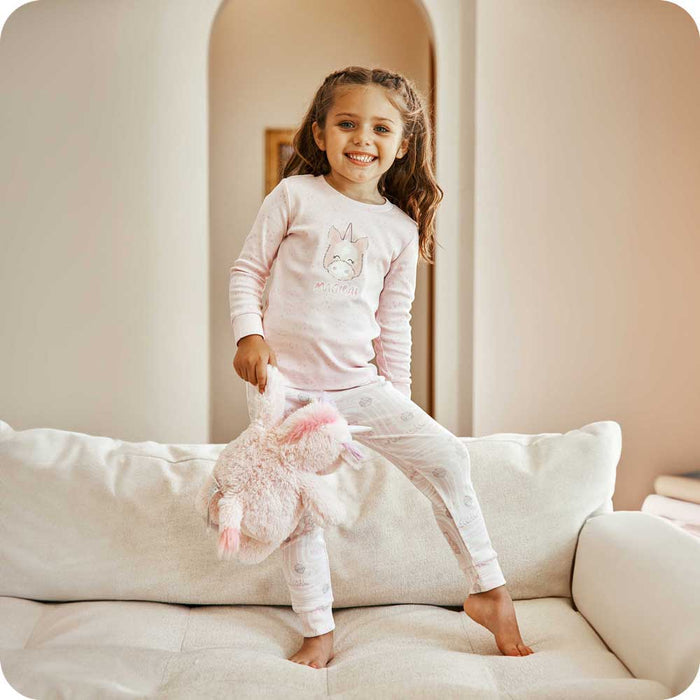 Child smiling while holding Soft Weighted Warmies Stuffed Animal and wearing Unicorn Pajamas - Warmies USA